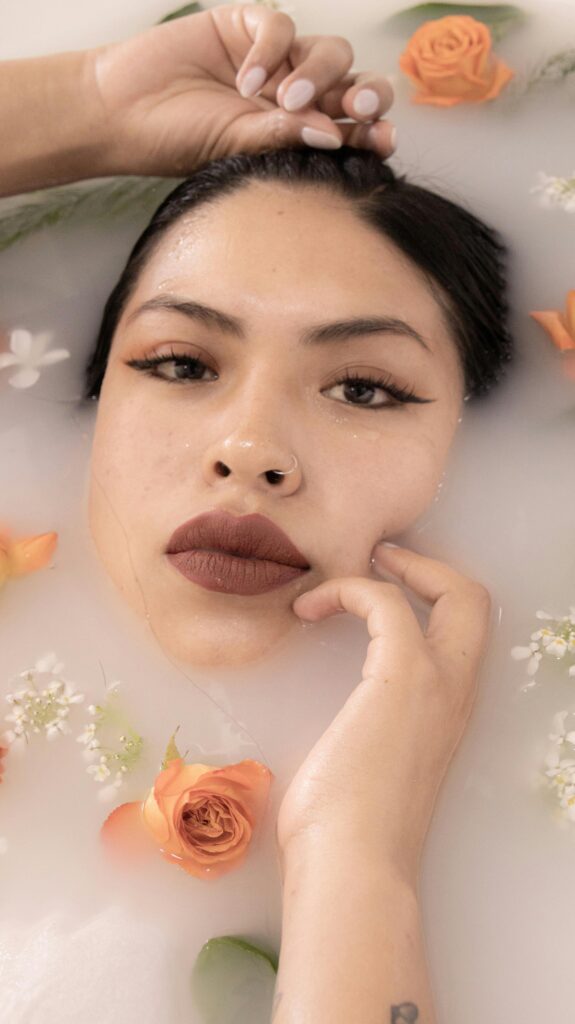 Elegant portrait of a woman submerged in a milk bath adorned with orange roses and greenery. Calm and serene